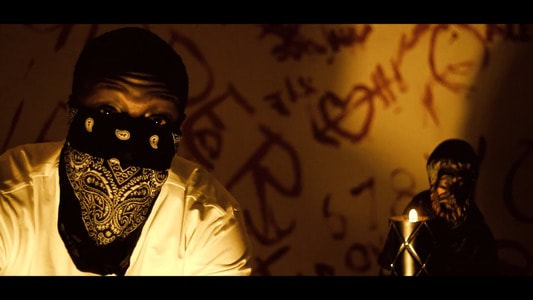 Hip hop artist Picasso De'France wearing a black bandana mask. Sitting with candles and angels.