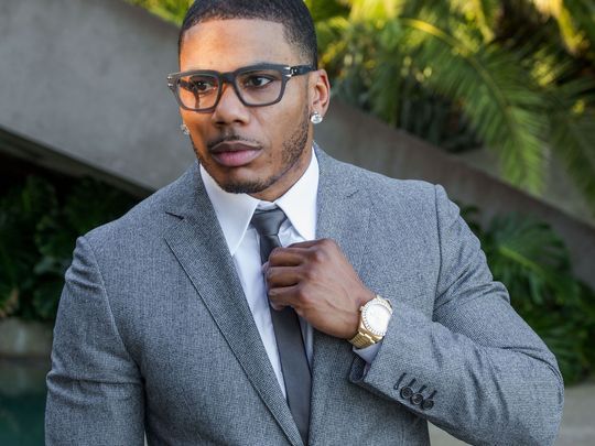 Rapper Nelly wearing glasses, large diamond earrings and a gray suit