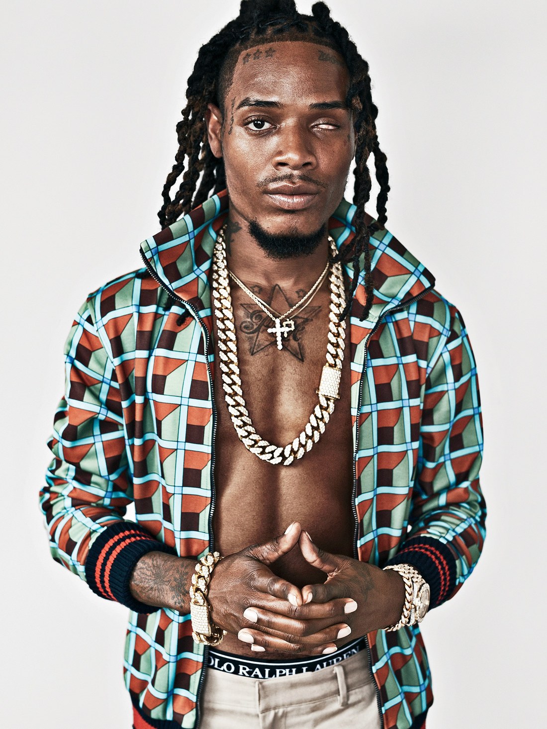 Rapper Fetty Wap wearing a print jacket, no shirt naked chest, gold bracelets on each wrist, gold watch and a 3 gold chains