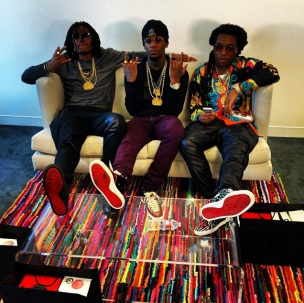 Rap group Migos wearing gold chains and Christian Louboutin shoes. Migos sitting on a cream couch and multi color rug with feet on glass coffee table.